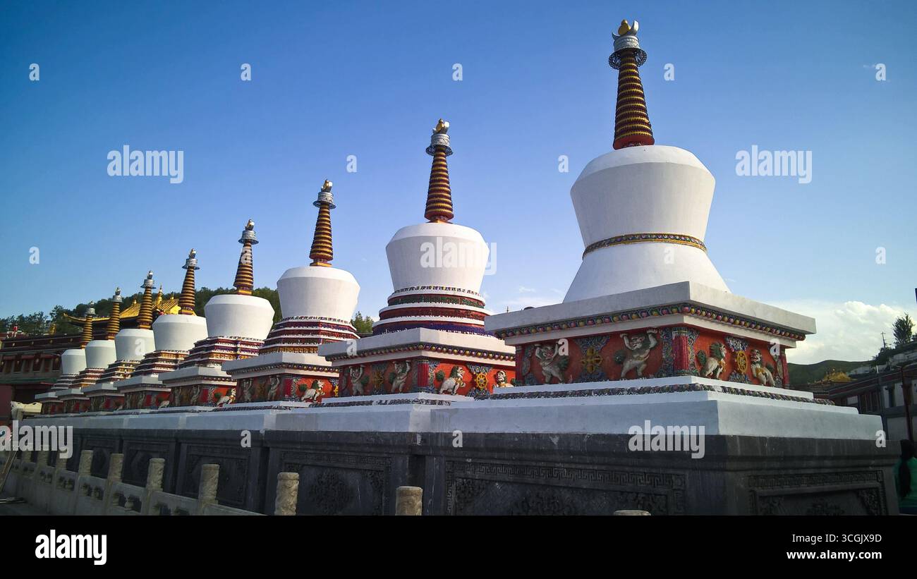 Viele weiße Stupas stehen in einer Reihe unter klarem Himmel und zeigen ihre geschichteten Strukturen und komplexen Basen mit einem Hauch von Bergen im Hintergrund Stockfoto