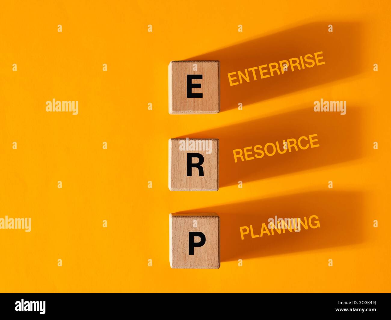 Hölzerne Würfel mit Buchstaben, die das Akronym ERP, Enterprise Resource Planning zusammensetzen, werfen ihren Schatten auf einen orangefarbenen Hintergrund Stockfoto