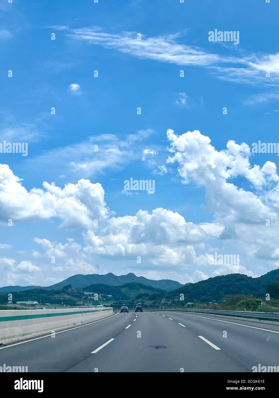 Sommerblick auf den Iksan-Pyeongtaek Expressway in Südkorea, mit einer leeren dreispurigen Autobahn, Bergen in der Ferne und großem Cumulus-Clou - Smartphone-aufgenommenes Stockfoto