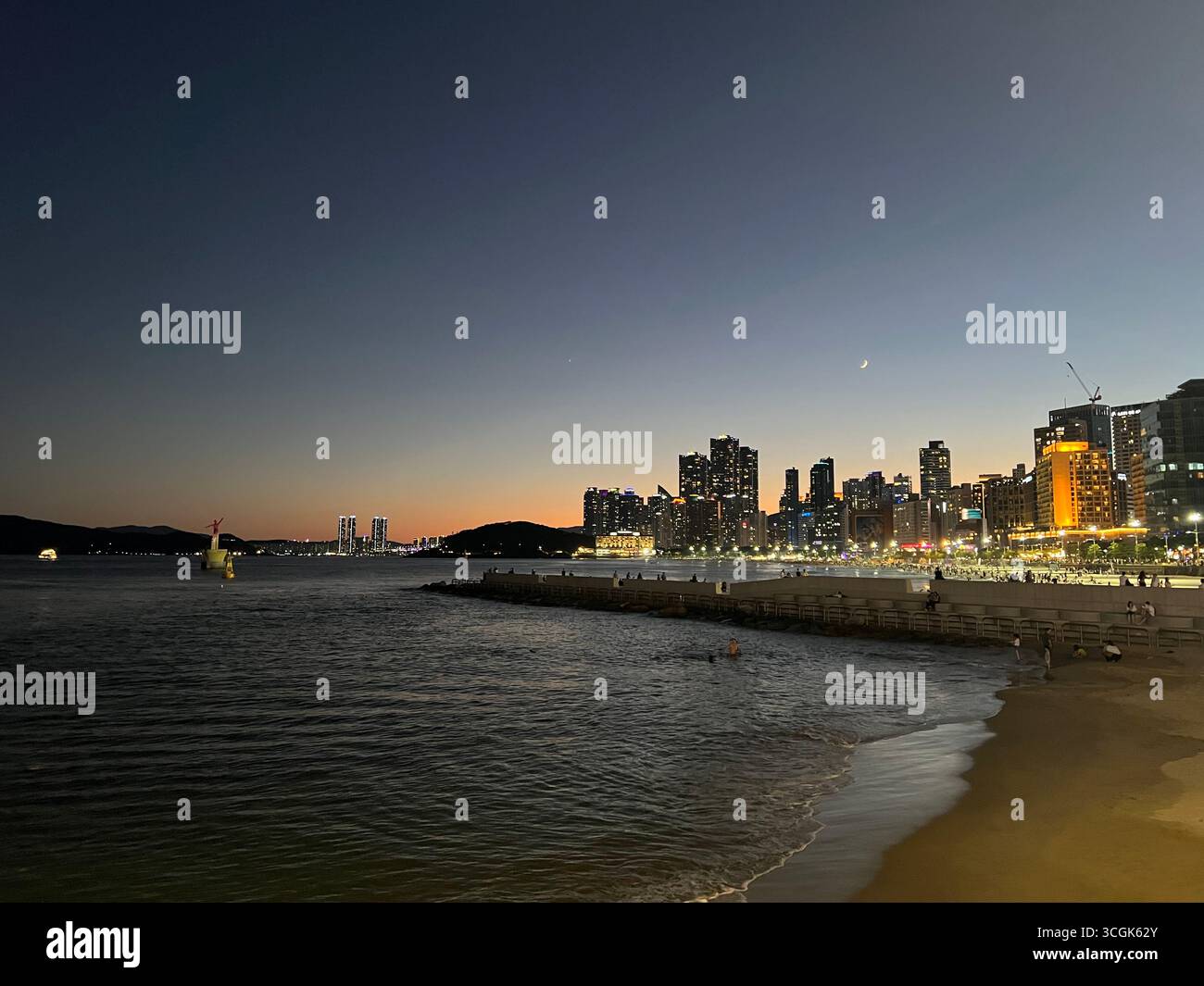 Nächtlicher Blick auf die Skyline von Haeundae in Busan, Südkorea, mit den Lichtern der Stadt über dem Meer, von Mipo aus gesehen. - Smartphone-aufgenommenes Stockfoto