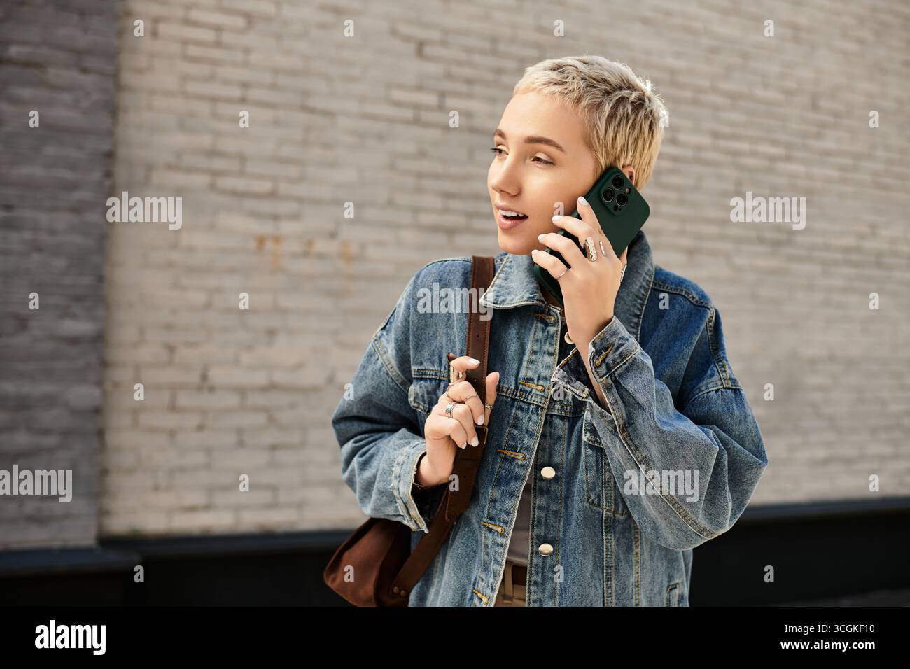 Eine junge Frau mit kurzen Haaren geht lässig nach draußen und lächelt, während sie am Telefon spricht. Stockfoto
