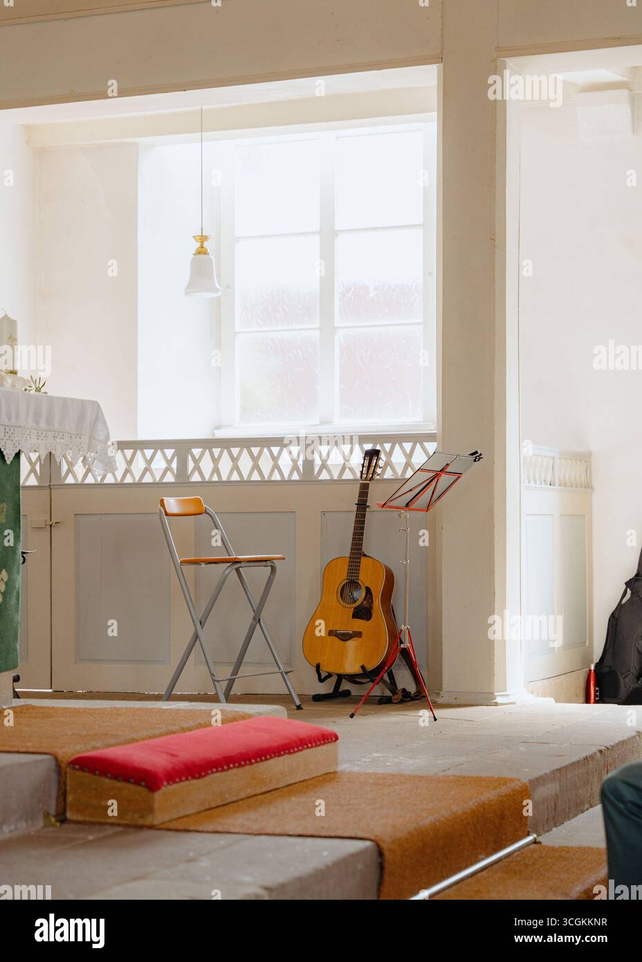 Sonnendurchfluteter Raum mit Akustikgitarre auf einem Ständer neben einem Klappstuhl und Notenständer. Die Lage bietet eine friedliche Atmosphäre, ideal Stockfoto