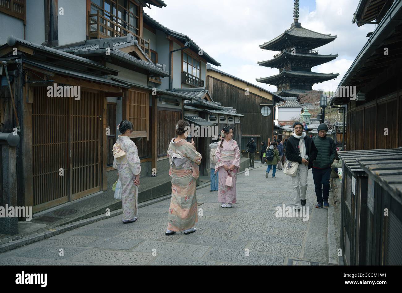 Frauen im Kimono halten für Fotos an den erhaltenen Straßen von Higashiyama, während die Yasaka-Pagode über den hölzernen Stadthäusern ragt Stockfoto