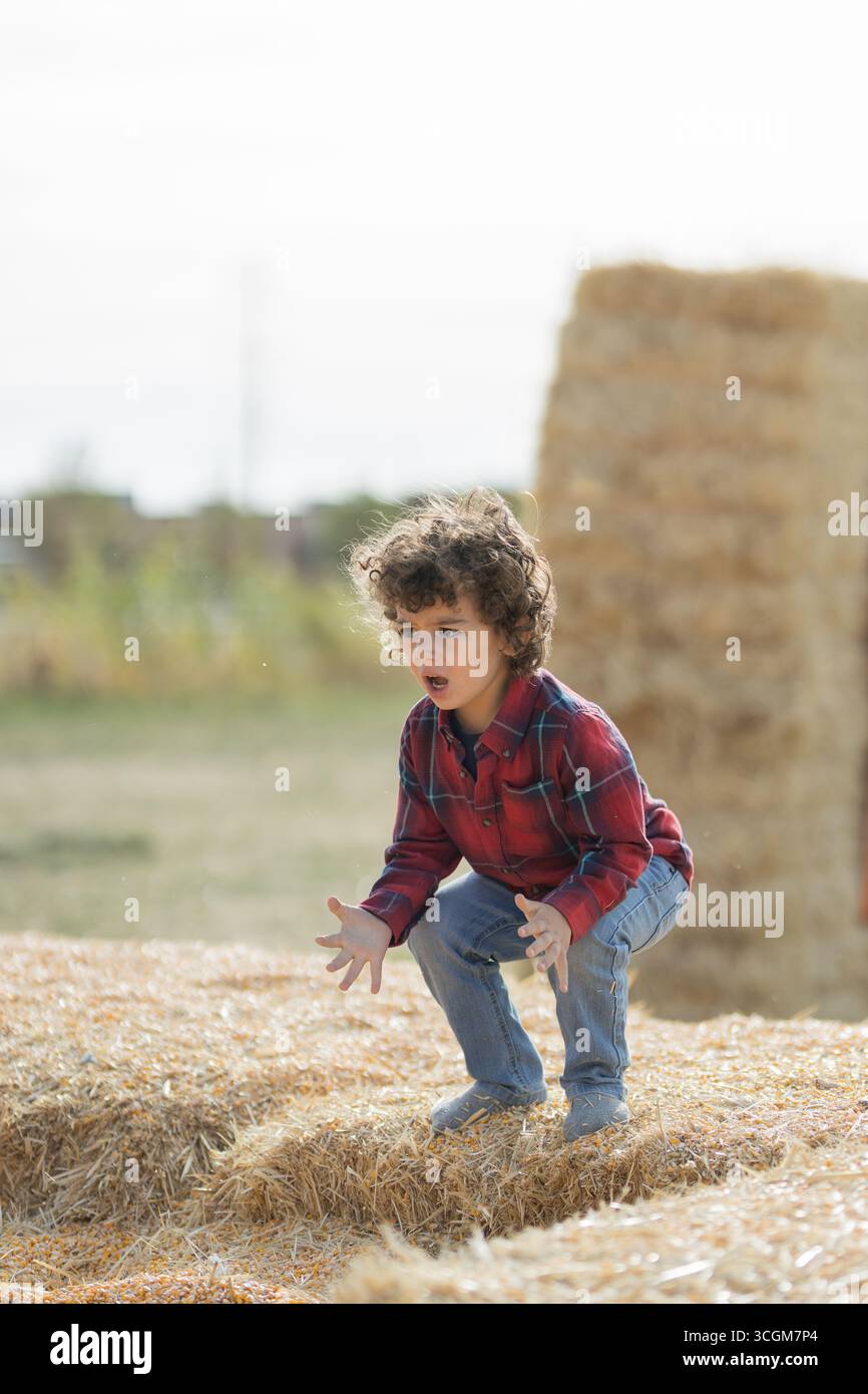 Kind in rotem kariertem Hemd, das draußen auf Heuballen hockt Stockfoto