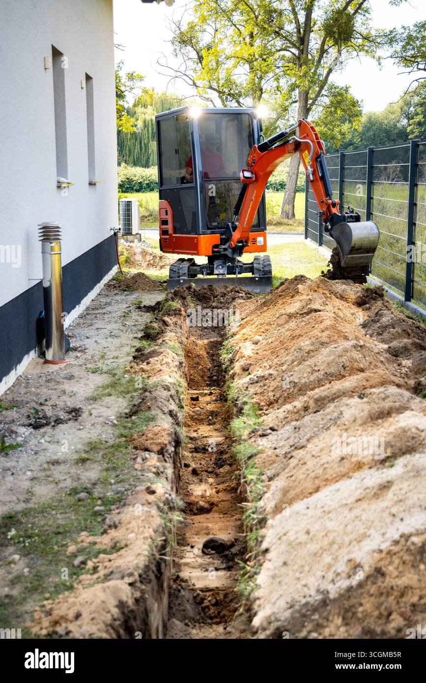 Minibagger, der einen Graben neben einem Einfamilienhaus gräbt Stockfoto