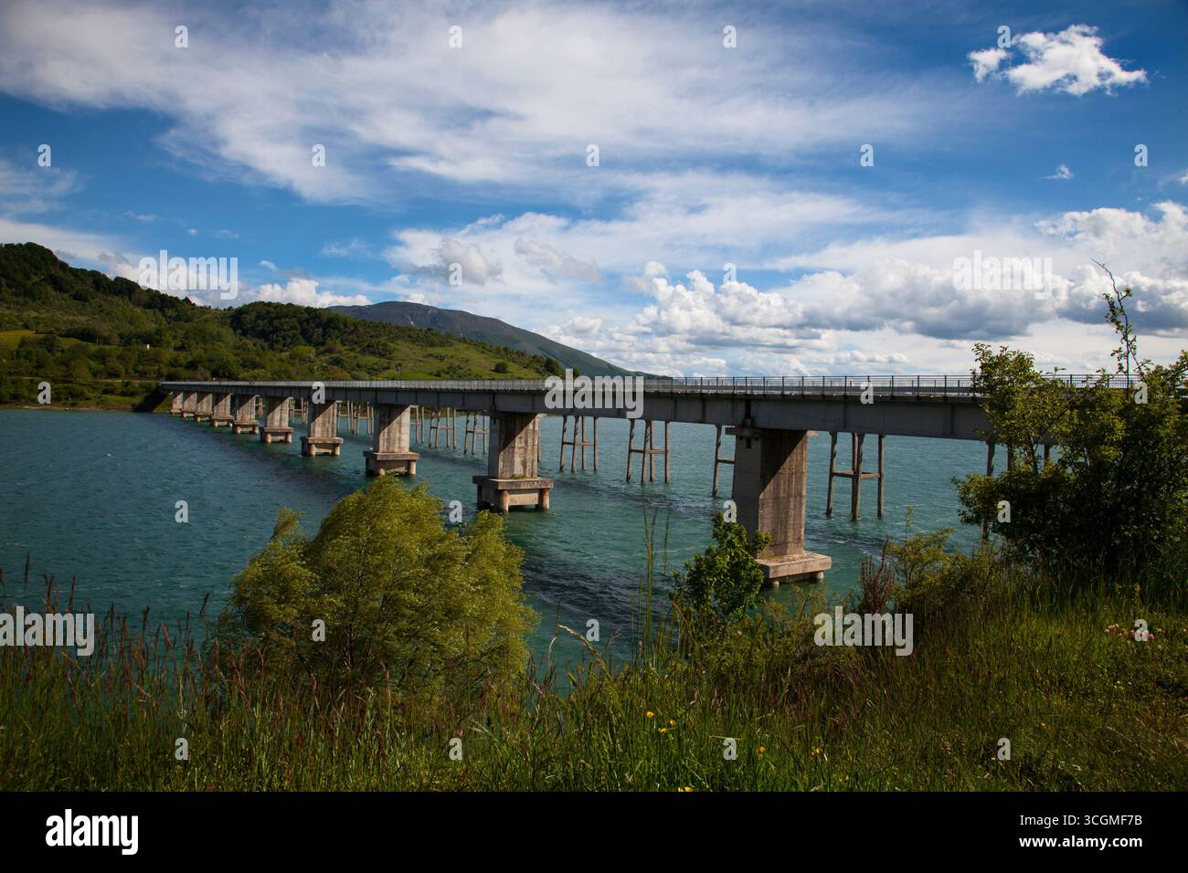 Eine Brücke über einen See mit Hügeln, Bäumen und grasbewachsenem Ufer Stockfoto