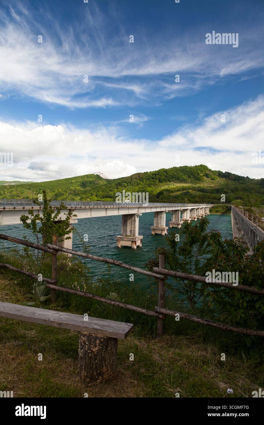 Eine Brücke über einen See mit Bergen und einem Berg im Hintergrund und einer Bank und einem Zaun im Vordergrund Stockfoto