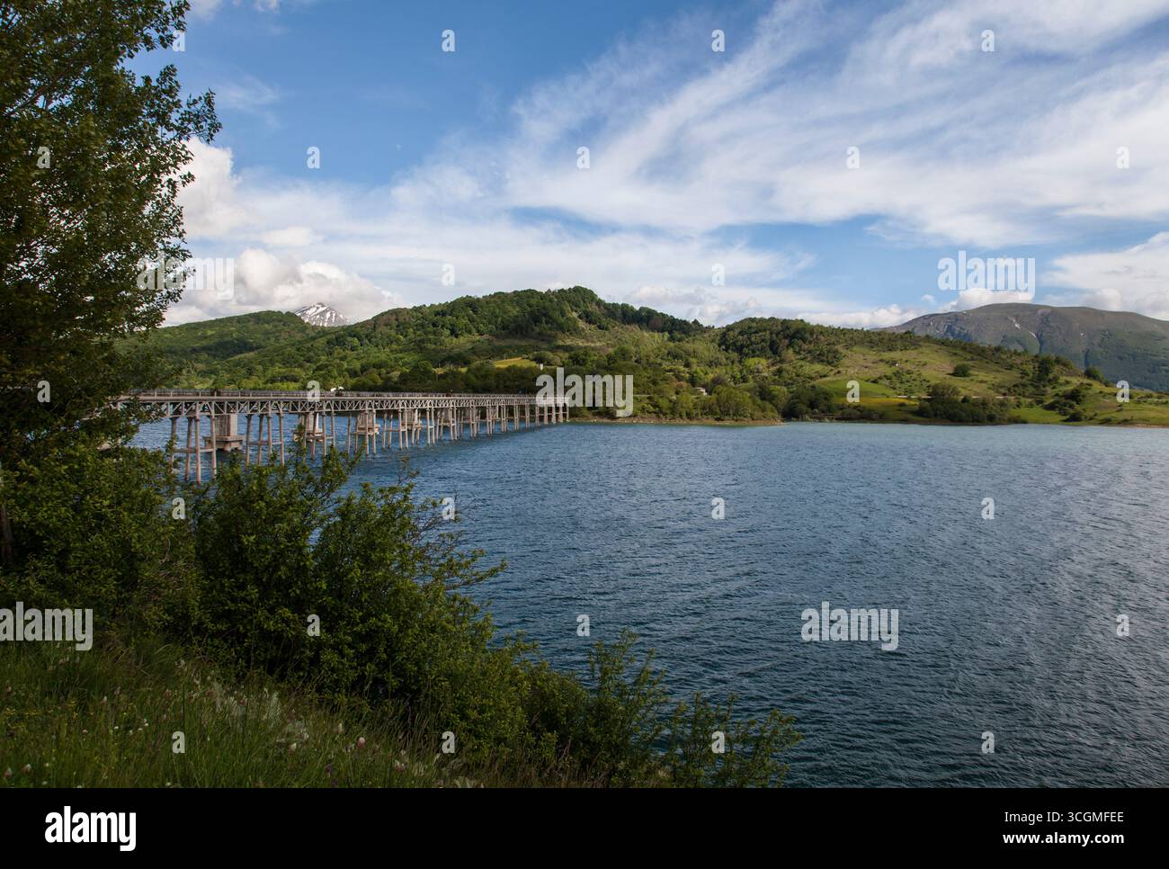 Eine Brücke über einen See mit Hügeln und einem schneebedeckten Berg in Italien Stockfoto