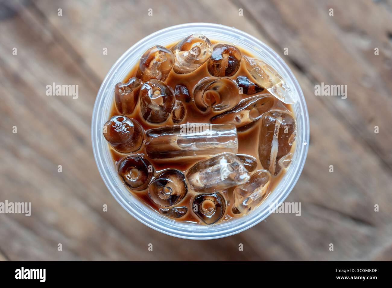 Blick auf Eiskaffee oder Latte von oben auf hölzernem Hintergrund. Schwarzer Kaffee mit Eis in Plastikglas, Nahaufnahme Stockfoto