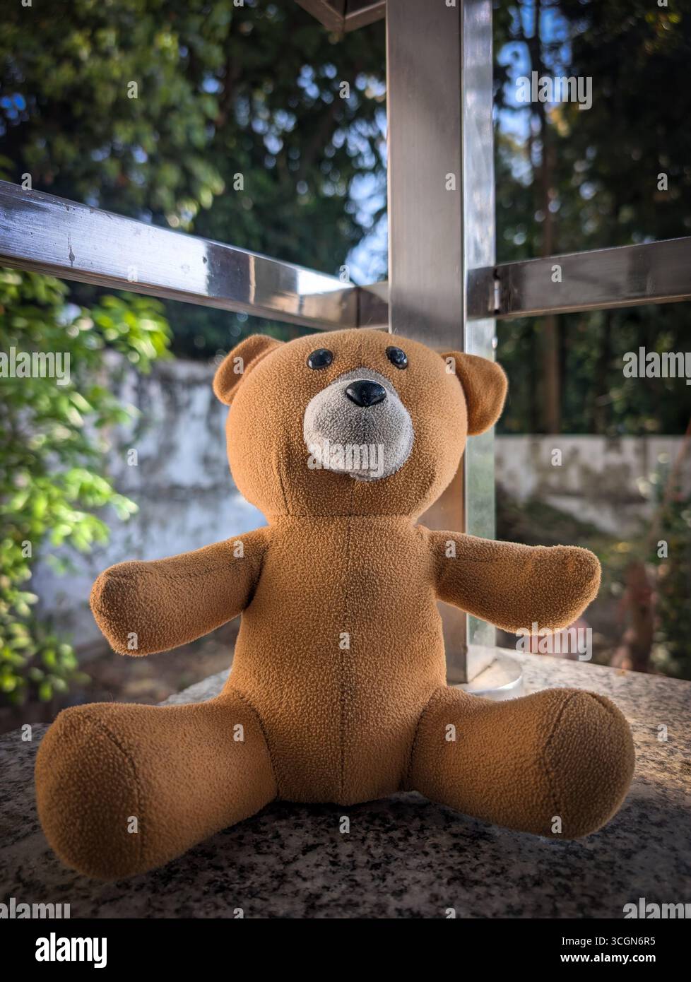 Ein niedlicher Teddybär, der auf einer Steinoberfläche sitzt, mit Grün im Hintergrund Stockfoto