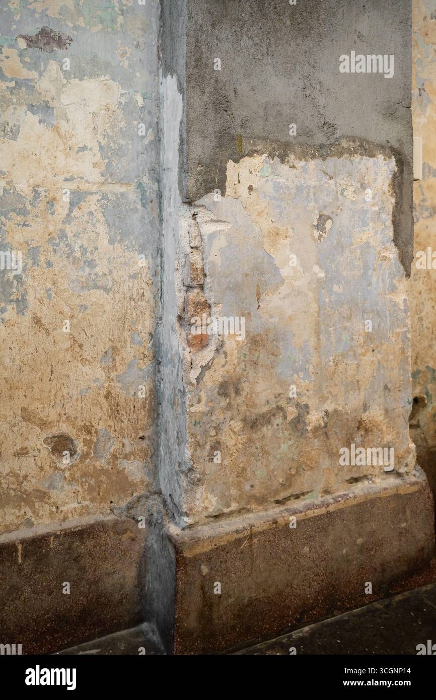 Ein Nahaufnahme-Bild zeigt eine detaillierte Ansicht einer verwitterten Wand mit abblätternder Farbe und freiliegendem Mörtel, die ihr strukturiertes und veraltetes Aussehen unterstreicht. Stockfoto