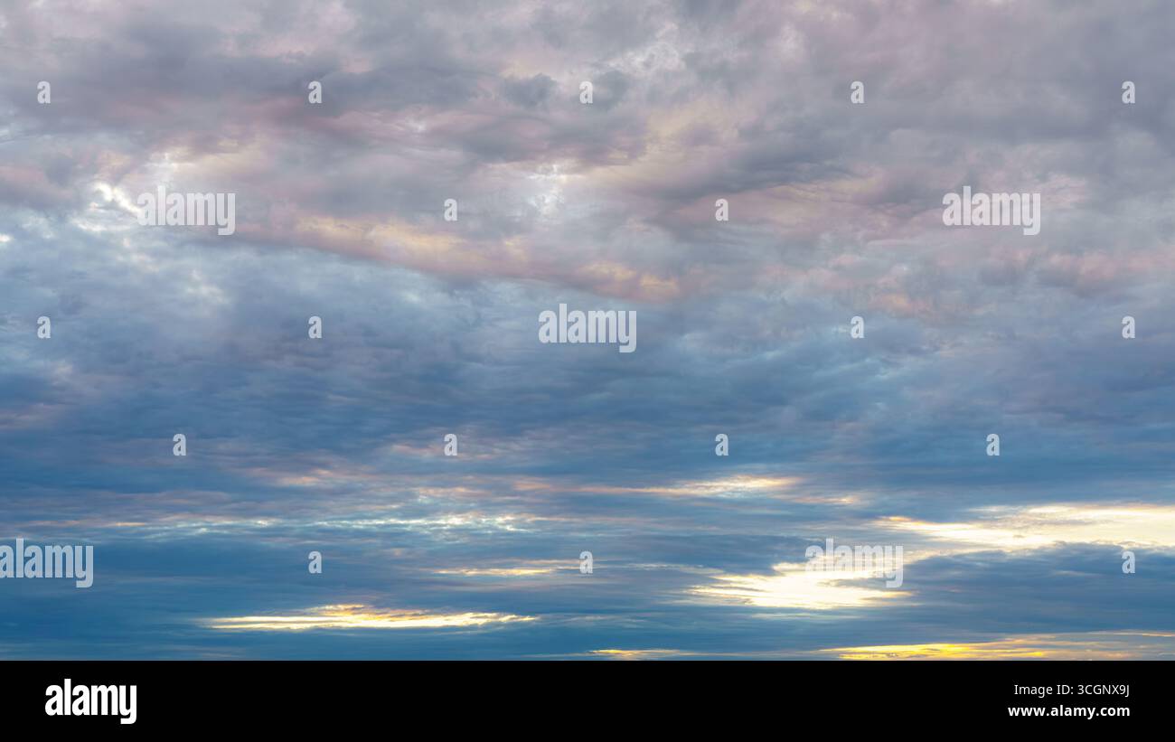 Überlagerte Altostratus- und Stratocumulus-Wolken erfüllen den Himmel bei Sonnenaufgang mit sanften Pastelltönen in Rosa, Blau und Gelb. Stockfoto