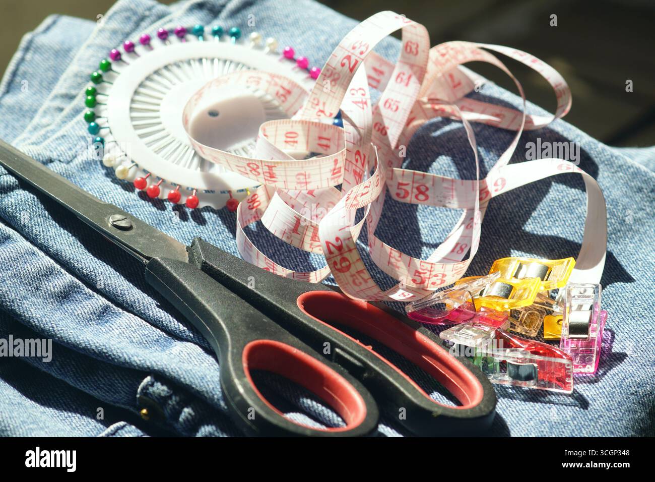 Nähset zu Hause für Reparatur- und Heimwerkerprojekte. Scheren, Nadeln, Quiltclips und Klebeband messen auf Denim. Symbol des praktischen Lebens und des Sparens Stockfoto