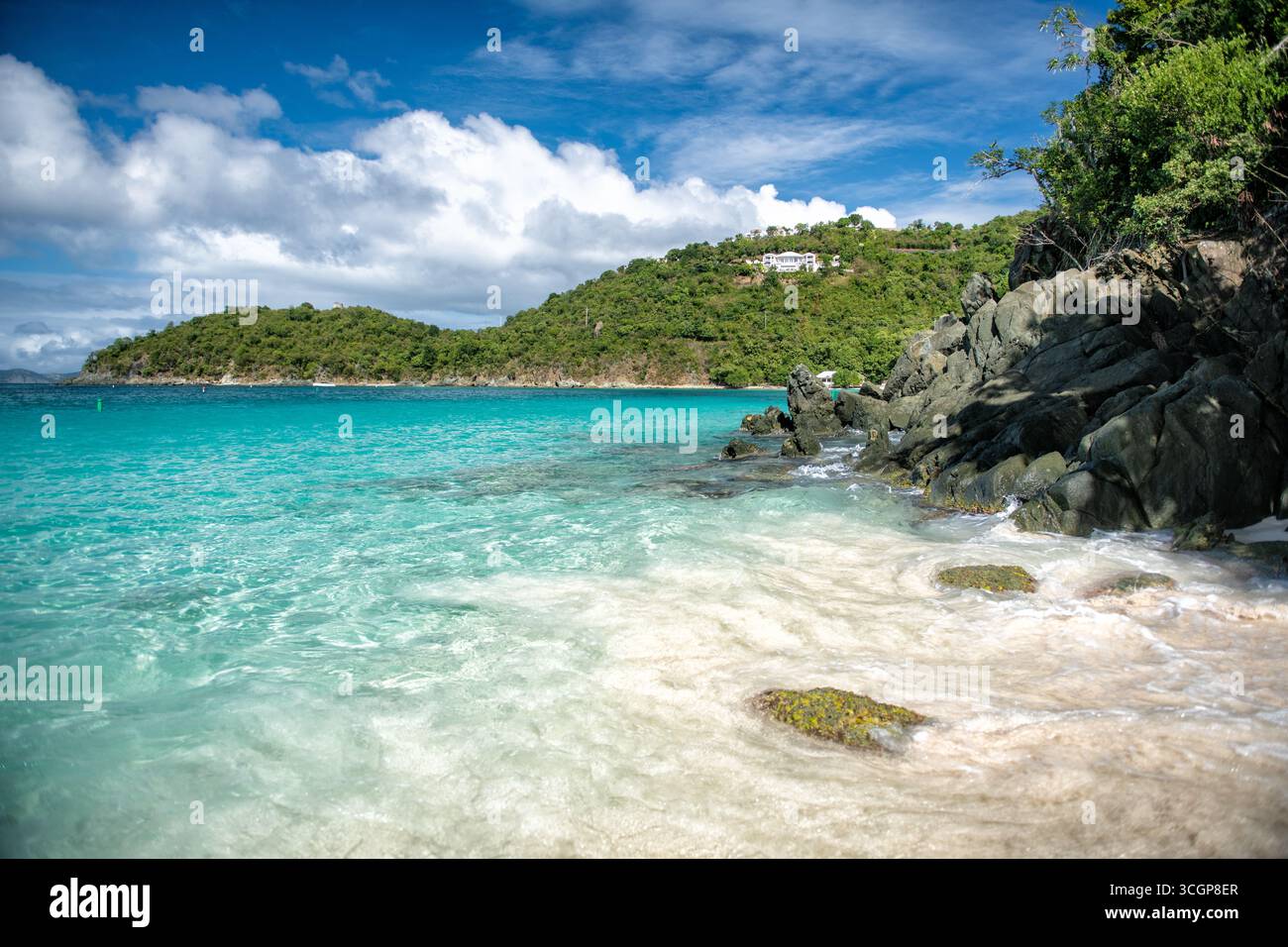 Hawksnest Bay St. John US Jungferninseln // HAWKSNEST BAY, St. John, U.S. Jungferninseln — das türkisfarbene Wasser liegt an der Hawksnest Bay, einem öffentlichen Strand auf der Insel St. John auf den US Jungferninseln. Die Bucht ist bekannt für ihr ruhiges, klares Wasser und die malerische, unbebaute Küste. Üppige grüne Hügel ragen hinter dem Strand auf, gespickt mit ein paar weißen Gebäuden. Hawksnest Bay ist Teil des Virgin Islands National Park und bewahrt seine natürliche Schönheit für Besucher. Der Park umfasst mehr als 60 % des St. John und bietet Möglichkeiten zum Schnorcheln, Wandern und Genießen der Karibik Stockfoto