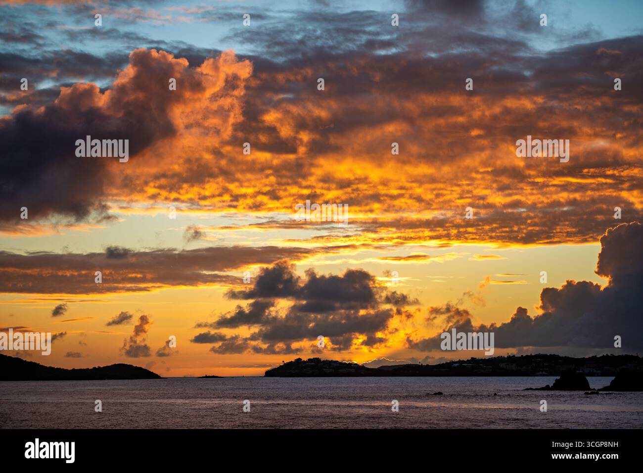 Sonnenuntergang über St. Thomas vom Galgen Point Cruz Bay St. John USVI // St. JOHN, USVI - Ein dramatischer Sonnenuntergang überzieht den Himmel mit leuchtenden Orange- und Gelbtönen über der Insel St. Thomas in der Ferne, vom Galgen Point in Cruz Bay aus gesehen. Die Szene fängt das ruhige Wasser des Karibischen Meeres ein, das die farbenfrohe Dämmerung reflektiert. St. John ist Teil der United States Virgin Islands, einem Gebiet, das für seine natürliche Schönheit und sein klares Wasser bekannt ist. Gallows Point ist ein beliebter Aussichtspunkt mit Panoramablick auf die umliegenden Inseln und die Meereslandschaft. Stockfoto