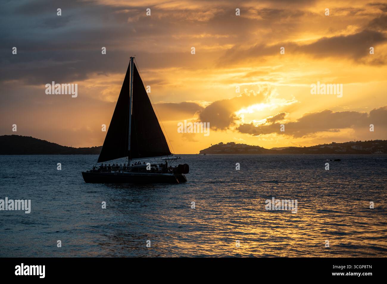 Sonnenuntergang über St. Thomas vom Galgen Point Cruz Bay St. John USVI // St. JOHN, USVI - Ein Segelboot fährt über das Wasser, während die Sonne über St. Thomas in der Ferne untergeht, vom Galgen Point in Cruz Bay aus gesehen. Der Himmel ist voller dramatischer Wolken, die von den warmen Tönen der untergehenden Sonne beleuchtet werden. St. John ist eine der Hauptinseln der amerikanischen Jungferninseln und liegt im Karibischen Meer. Die U.S. Jungferninseln sind ein nicht eingemeindetes Territorium der Vereinigten Staaten. Stockfoto