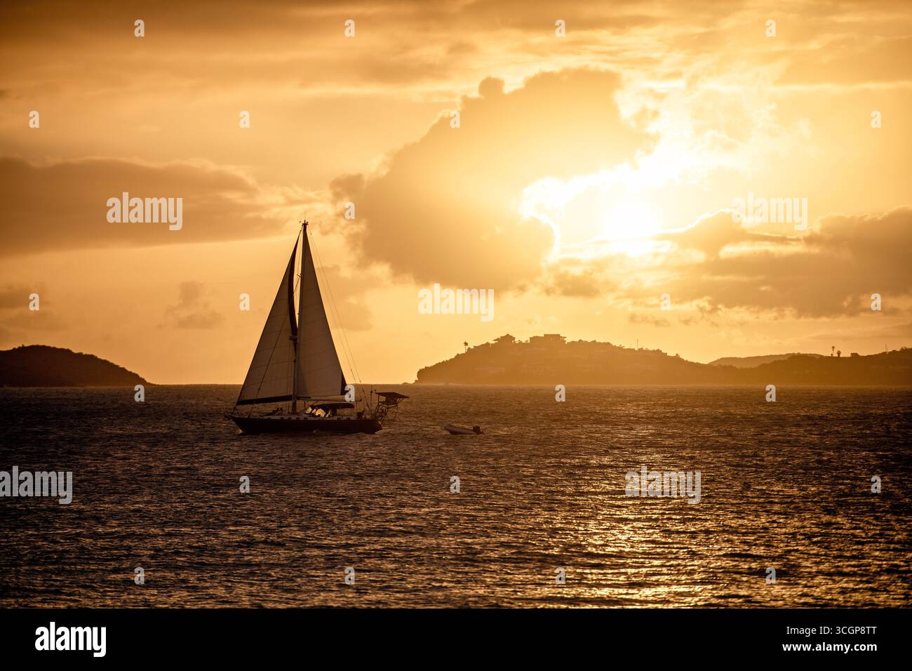 Segelboot auf dem Wasser bei Sonnenuntergang in der Nähe von St. Thomas ab St. JOHN USVI // St. JOHN, USVI — Ein Segelboot navigiert durch die Gewässer vor St. John auf den US-Jungferninseln, während die Sonne untergeht und einen warmen goldenen Glanz über den Himmel wirft. In der Ferne ist die Insel St. Thomas am Horizont sichtbar. Der Aussichtspunkt für diese Szene ist Gallows Point in Cruz Bay, ein beliebter Ort auf St. John, der für seine malerischen Ausblicke bekannt ist. Die U.S. Jungferninseln sind eine Gruppe von Inseln im Karibischen Meer, die ein nicht eingemeindetes US-Territorium bilden. Stockfoto