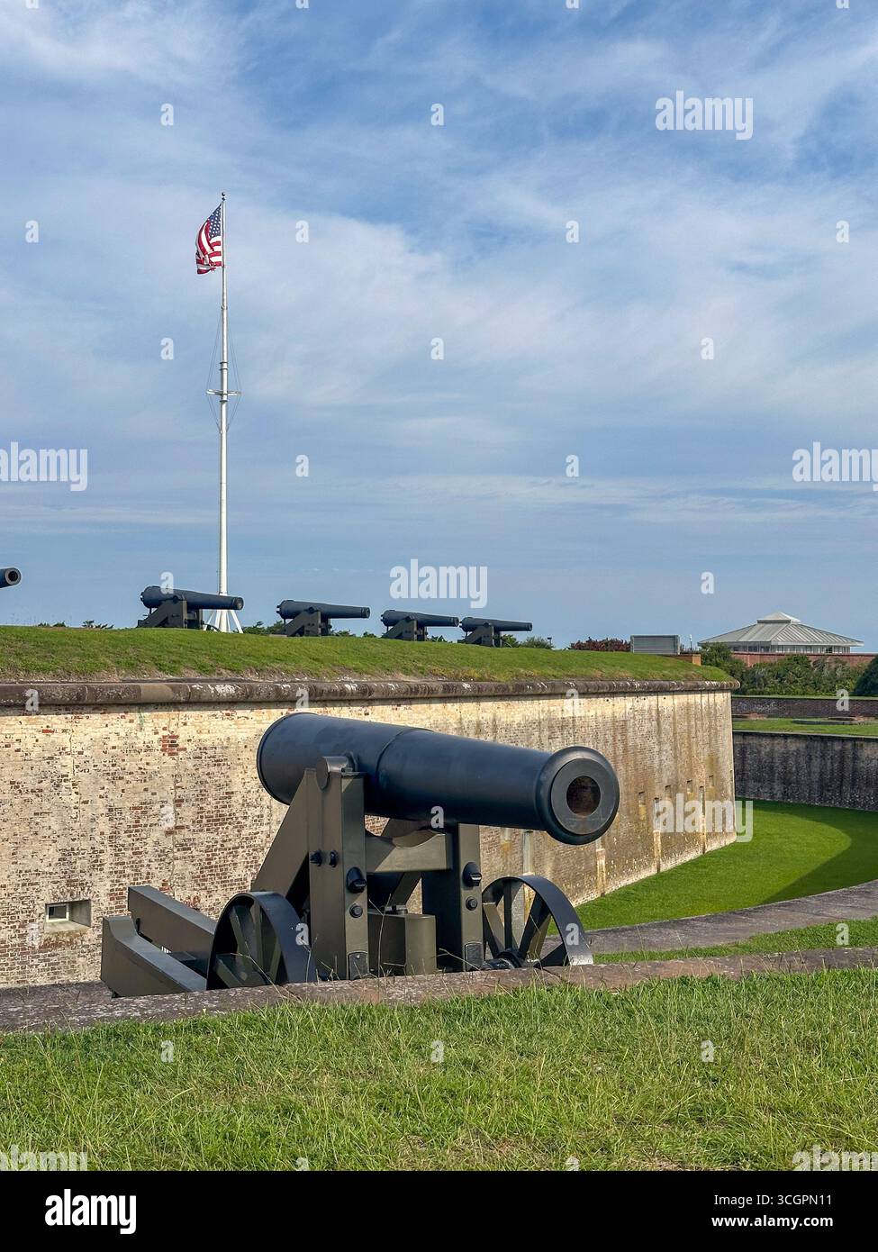Eine Reihe historischer Küstenverteidigungskanonen säumt die grasbewachsenen Stadtmauern von Fort Macon in North Carolina mit amerikanischer Flagge Stockfoto