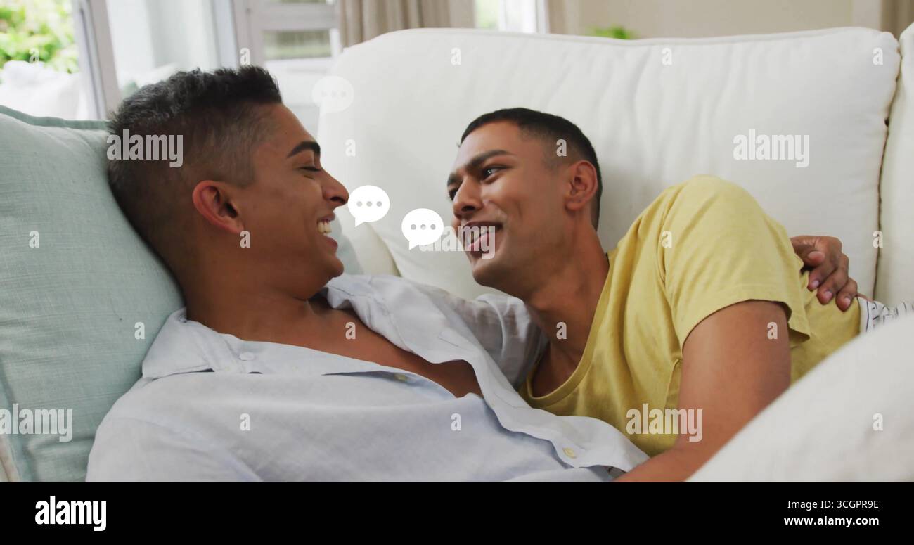 Liegen liegende indische Männer mit legeren Oberteilen zu Hause auf weißem Sofa mit Sprechblasen in der Nähe des Fensters Stockfoto