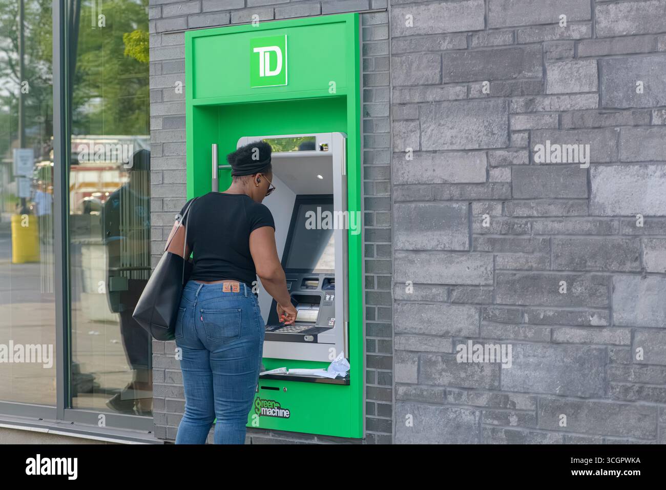 Eine Frau interagiert mit einem TD Green Machine Geldautomaten, der neben einer Glaswand und einem Backsteingebäude steht. Stockfoto