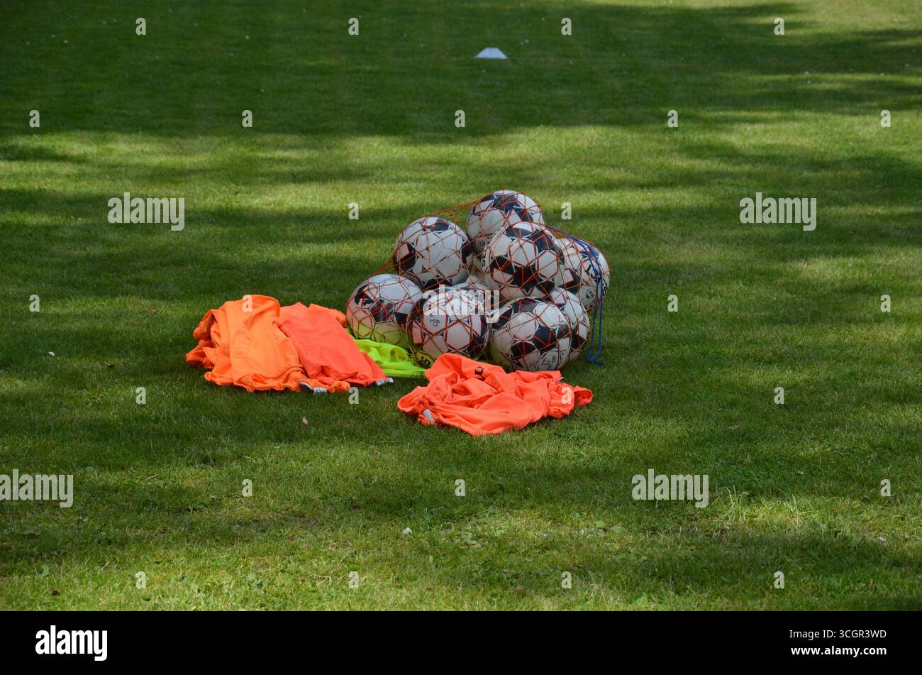 Fußballbälle und Trainingstrikots sind auf dem Spielfeld verteilt und bereit für das Training. Stockfoto