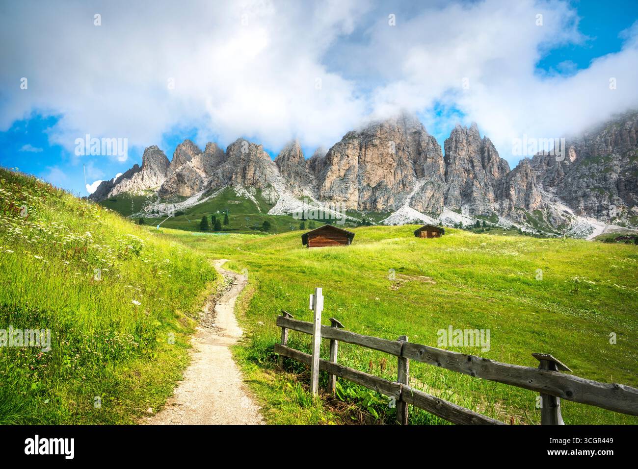 Malerischer Wanderweg mit Holzzaun führt zu dramatischen Kalkgipfeln durch grüne Almwiesen am Grödner Passo, UNESCO-Weltkulturerbe der Dolomiten, Süden Stockfoto