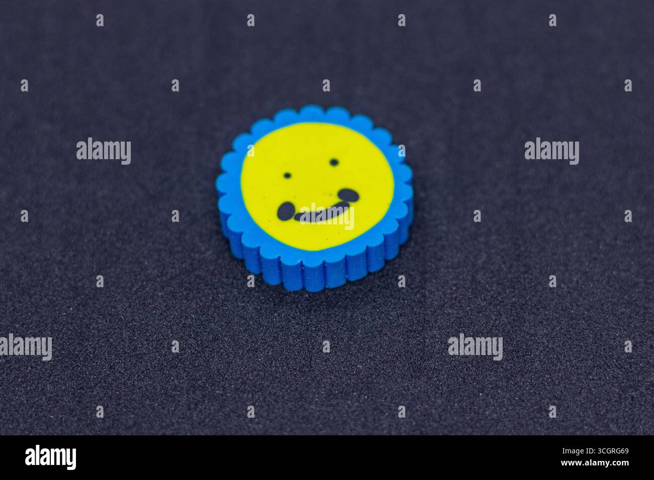 Niedlicher Smiley Gesichtsradierer in Blau und Gelb auf schwarzem Hintergrund Stockfoto