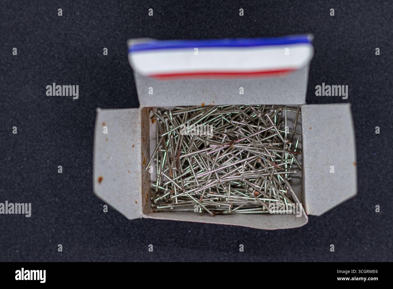 Offene Kartonbox gefüllt mit Metallstiften auf schwarzer Oberfläche Stockfoto