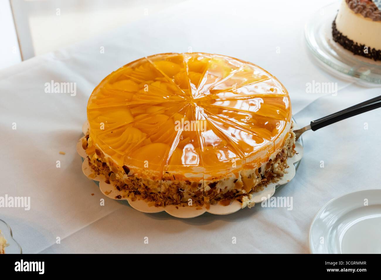 Deutscher Obstkuchen mit Pfirsich, Gelee und Mandeln auf einem Tisch. Nahaufnahme des süßen Desserts, geschnitten. Essen, um ein Ereignis zu feiern. Beliebtes Gebäck. Stockfoto