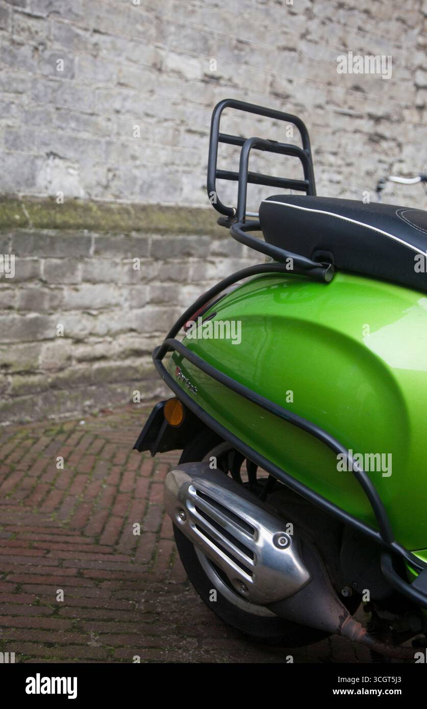 Eine grüne Vespa, teilweise gesehen, mit einem Schloss, Gepäckablage mit einem traditionellen Stadthintergrund Stockfoto