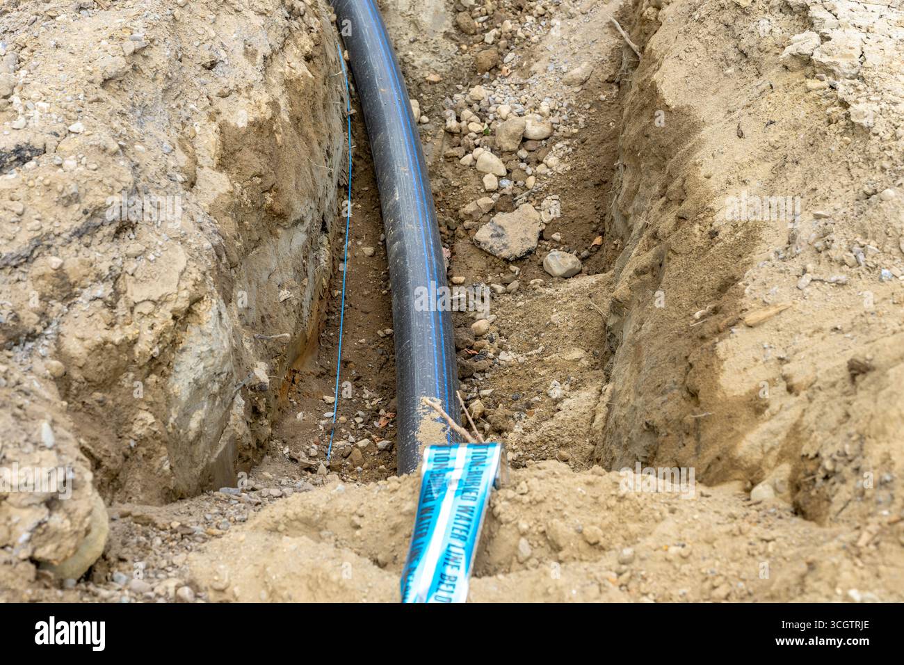 Neue Wasserleitung aus schwarzem Polyethylen, PE, wird in einem Graben mit blauem unterirdischem, nachweisbarem Sicherheitsband installiert. Stockfoto