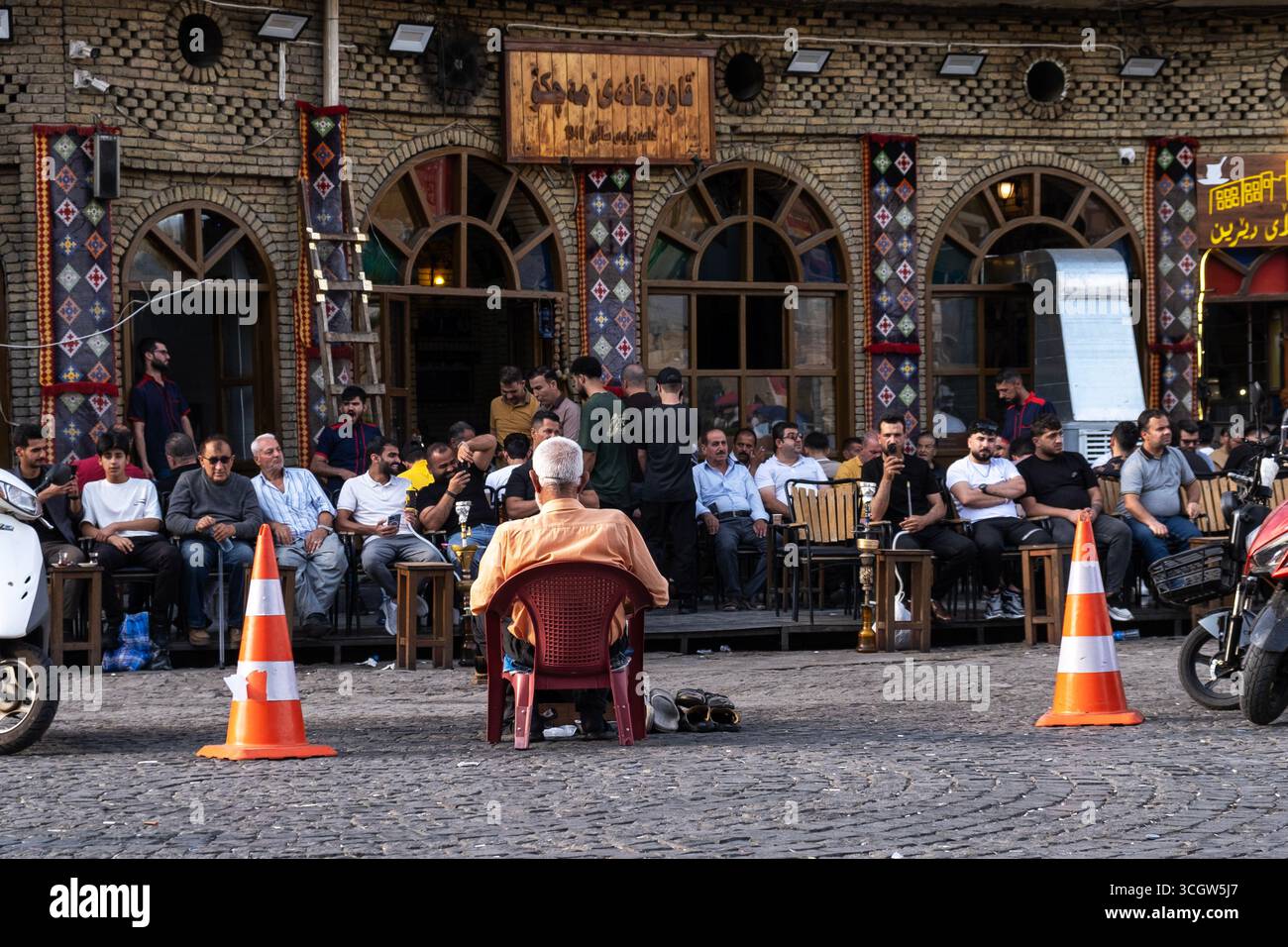Ein Mann, der die Schuhe der Menschen malt, sitzt gegen eine Gruppe von Schuhen namens Teehaus namens Machko Erbil Stockfoto
