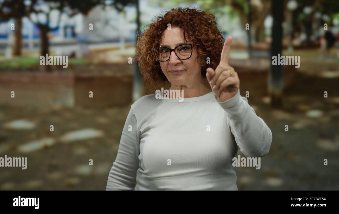 Frau gibt Missbilligung im Park, trägt Brille mit brünetten lockigen Haaren im Hintergrund im Freien, was auf einen nachdenklichen Moment während sunn hindeutet Stockfoto