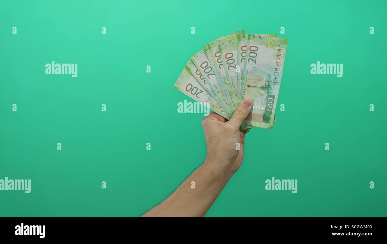 Männliche Hand, die russische Rubelscheine isoliert vor einem leuchtenden grünen Hintergrund hält, zeigt das Finanzkonzept in einem einfachen, aber auffälligen mann Stockfoto