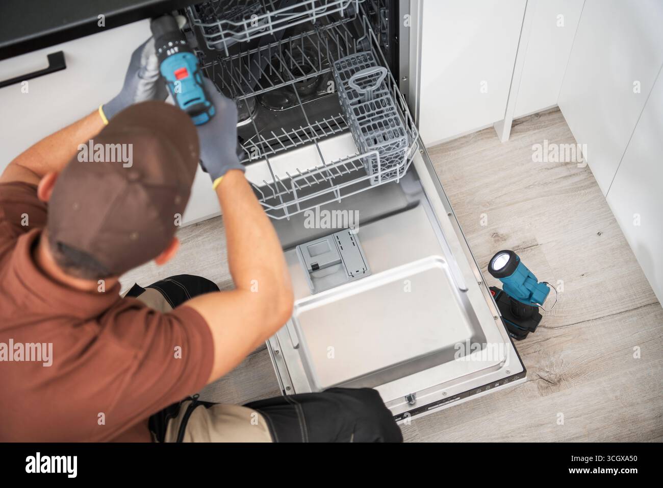 Ein Techniker arbeitet an der Reparatur eines Geschirrspülers in einer modernen Küche, verwendet einen Schraubendreher und untersucht das Gerät sorgfältig. Stockfoto