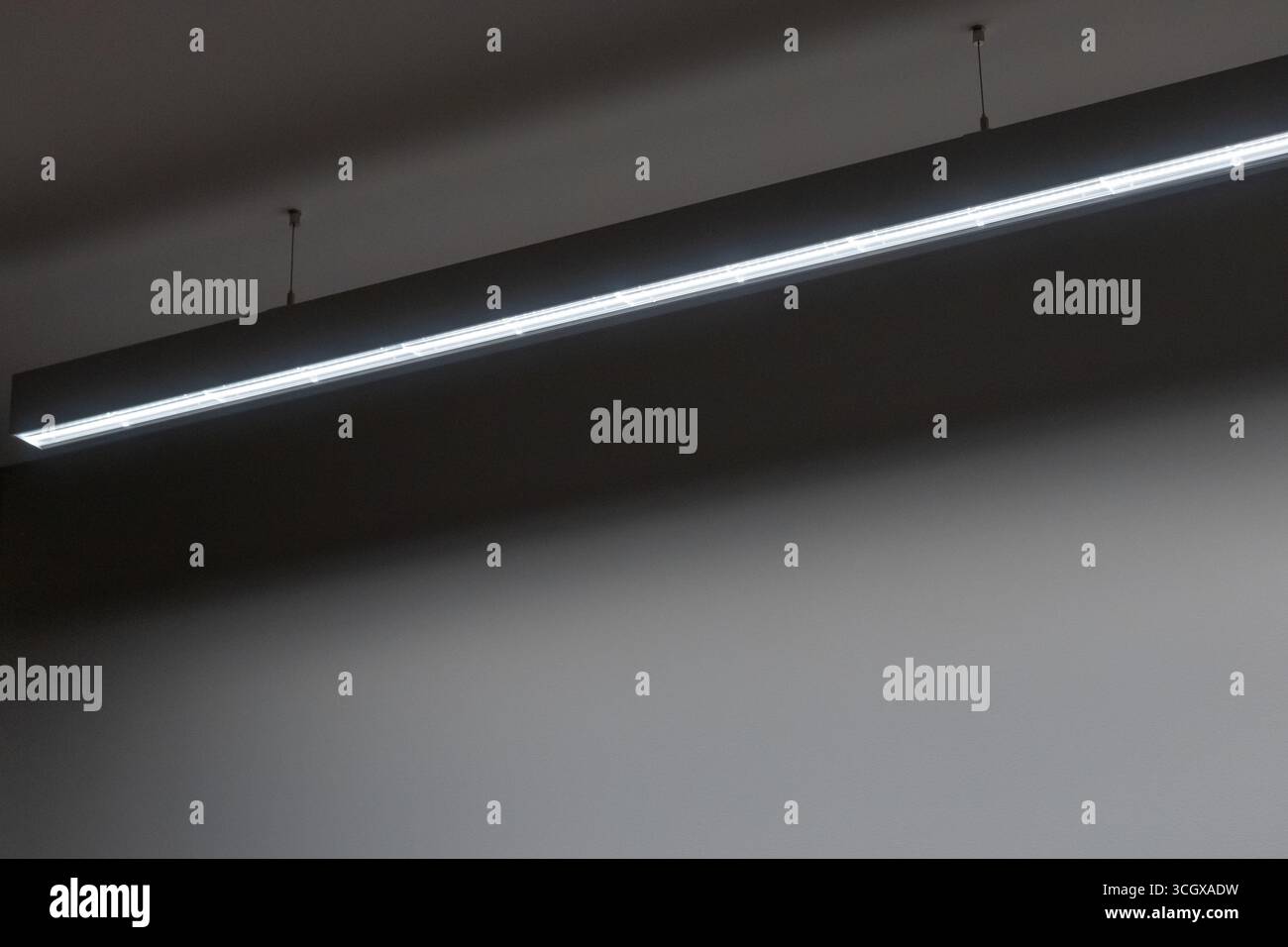 Hängende lineare Profilbeleuchtung mit prismatischer Abdeckung für eine gleichmäßige und blendfreie Beleuchtung, ideal für moderne Büroumgebungen Stockfoto