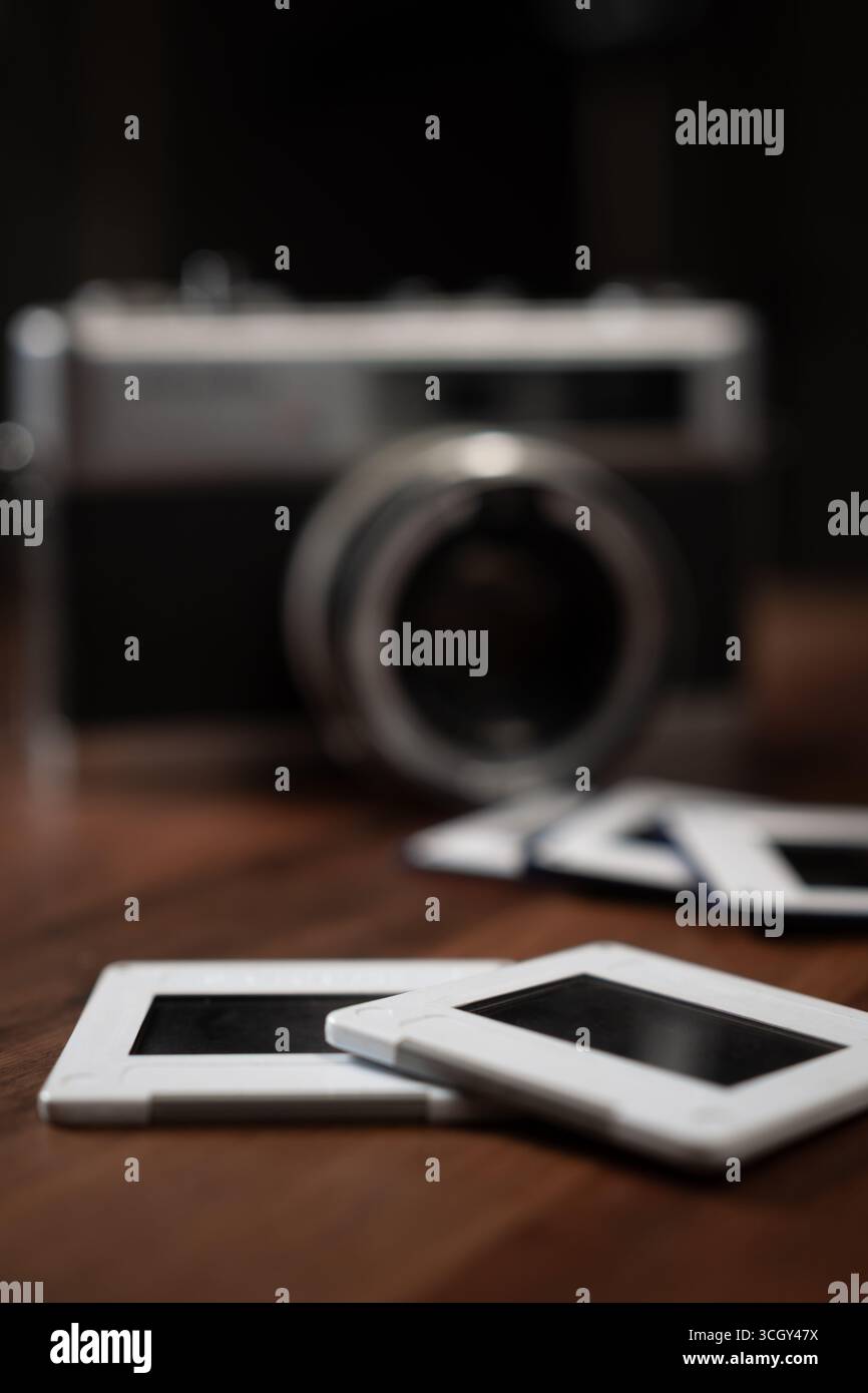 Nahaufnahme von Fotodias auf einem Holztisch mit einer alten Kamera im Hintergrund, die Nostalgie und Erinnerungen an vergangene Reisen weckt Stockfoto