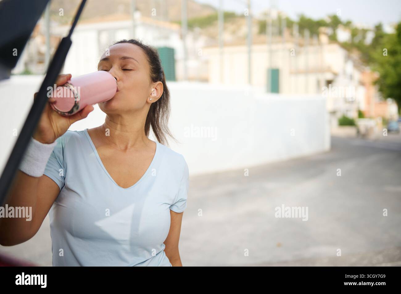 Eine Frau erfrischt sich an einem sonnigen Tag im Freien mit einem Getränk aus einer rosa Flasche. Sie wirkt aktiv und entspannt, zeigt ein Gefühl des Gleichgewichts Stockfoto