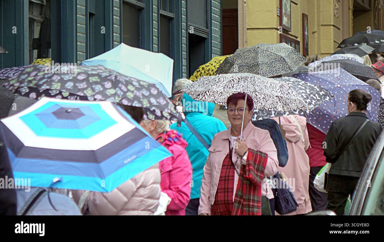Glasgow, Schottland, Großbritannien. 30. August 2025. Wetter in Großbritannien: Der Sommer verschwand, als starker Regen die Hitzewelle im Stadtzentrum ablöste. Die Damen strömen und stellen sich in die Warteschlange für die Bay City Rollers Musical „Rollers Forever“ im Pavillon Theater. Credit Gerard Ferry/Alamy Live News Stockfoto