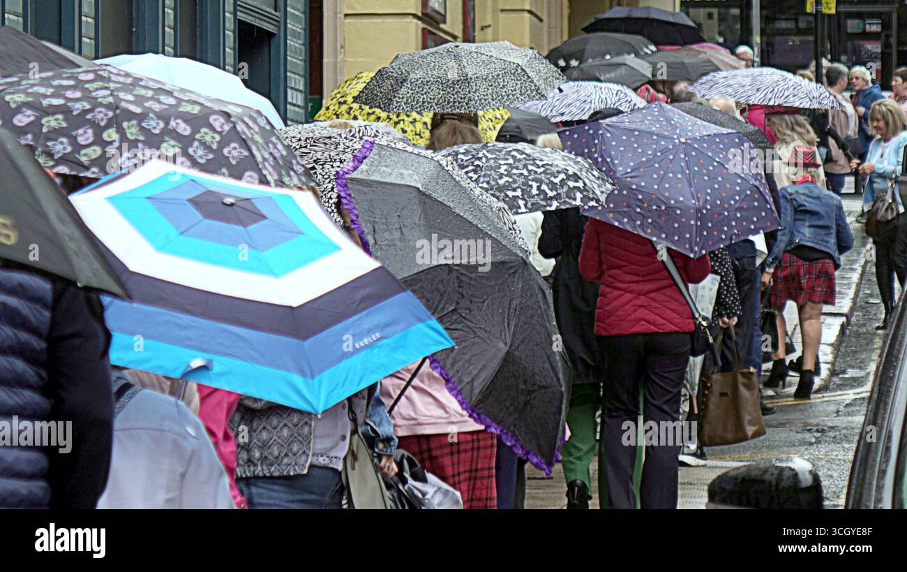 Glasgow, Schottland, Großbritannien. 30. August 2025. Wetter in Großbritannien: Der Sommer verschwand, als starker Regen die Hitzewelle im Stadtzentrum ablöste. Die Damen strömen und stellen sich in die Warteschlange für die Bay City Rollers Musical „Rollers Forever“ im Pavillon Theater. Credit Gerard Ferry/Alamy Live News Stockfoto