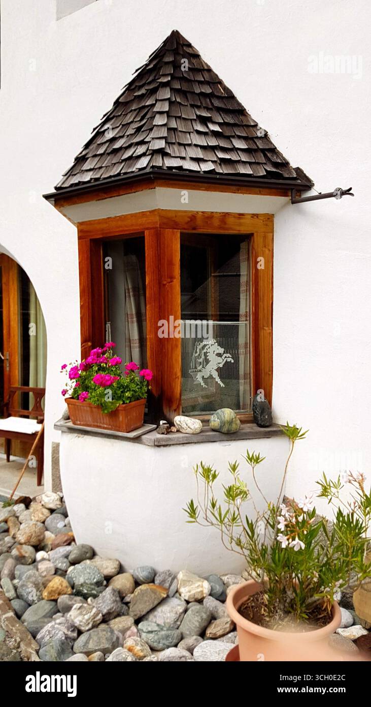 Typisch Engadiner Haus Erkerfenster mit rustikalen Holzfensterrahmen, dekoriert mit schönen rosa Blumen, Schweiz Stockfoto
