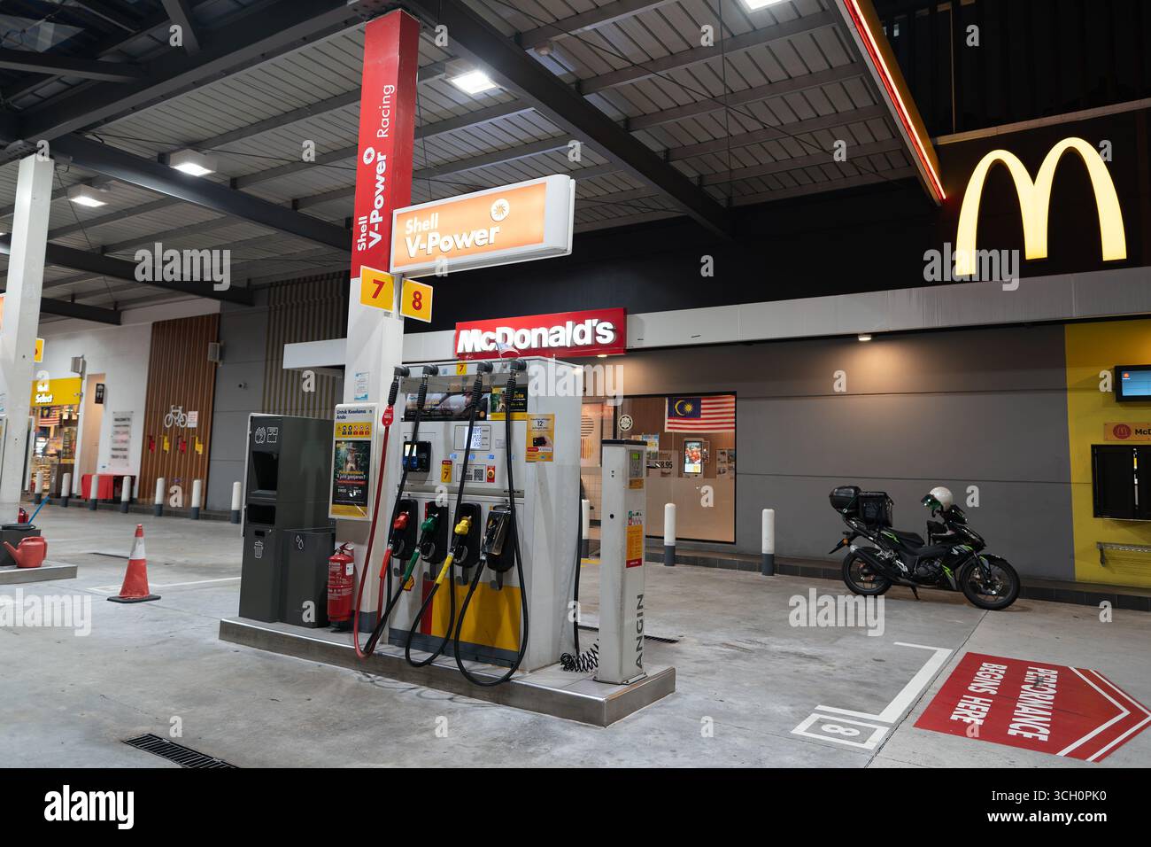 Kuala Lumpur, Malaysia - 17. September 2024: Eine Shell V-Power-Benzinpumpe an einer Tankstelle in der Nacht, mit einem McDonald's und einem geparkten Motorrad in der Ba Stockfoto