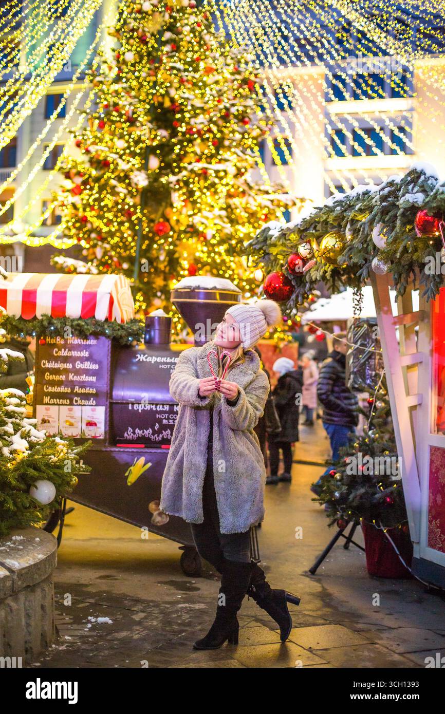 moskau, russland, 12.01.2020 Eine glückliche Frau steht mit Zuckerrohrherzen auf einem hell erleuchteten Weihnachtsmarkt. Festliche Feiertage. Stockfoto