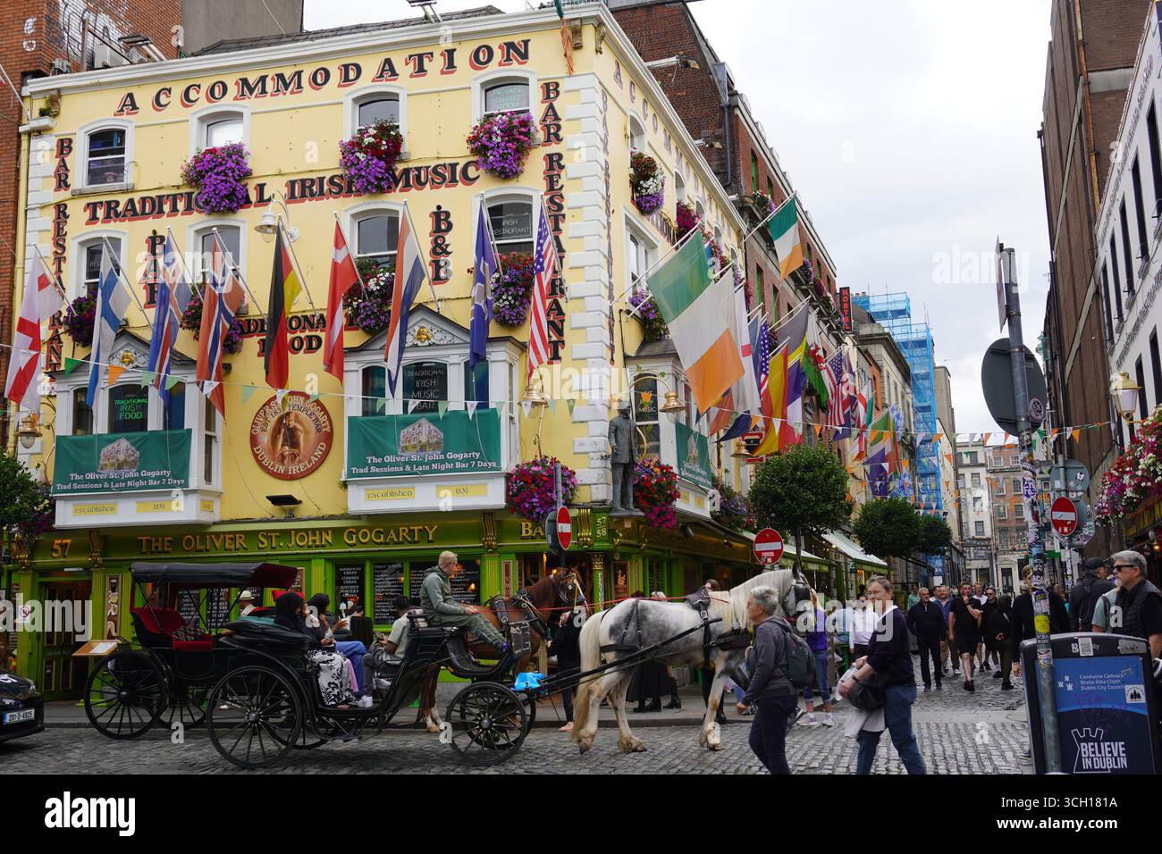 Ein traditioneller Pub in der Temple Bar Gegend von Dublin, Irland, ist mit Fahnen und Blumen geschmückt, an dem eine Pferdekutsche vorbeifährt. Stockfoto