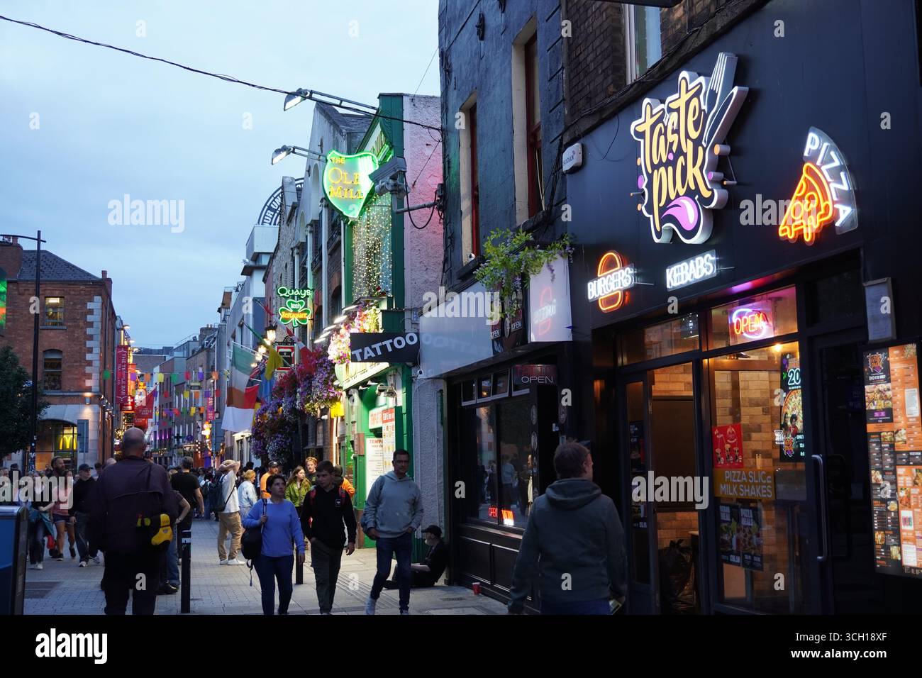 Dublins Temple Bar-Viertel erwacht in der Abenddämmerung zum Leben, während farbenfrohe Neonschilder belebte Straßen voller Einheimischer und Touristen erleuchten. Stockfoto