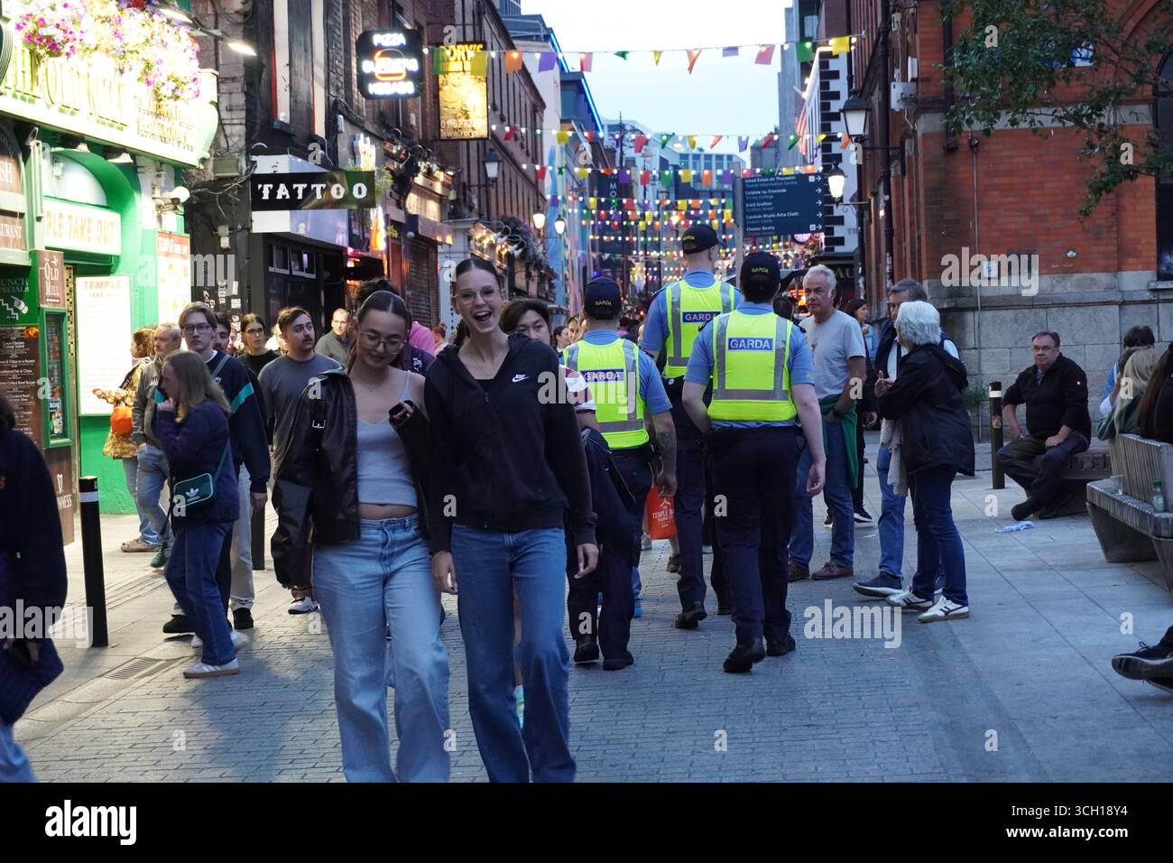 Zwei lächelnde Freunde spazieren durch eine belebte Straße in Dublin und halten einen ehrlichen Moment der Freude in der lebhaften Atmosphäre der Stadt fest. Stockfoto