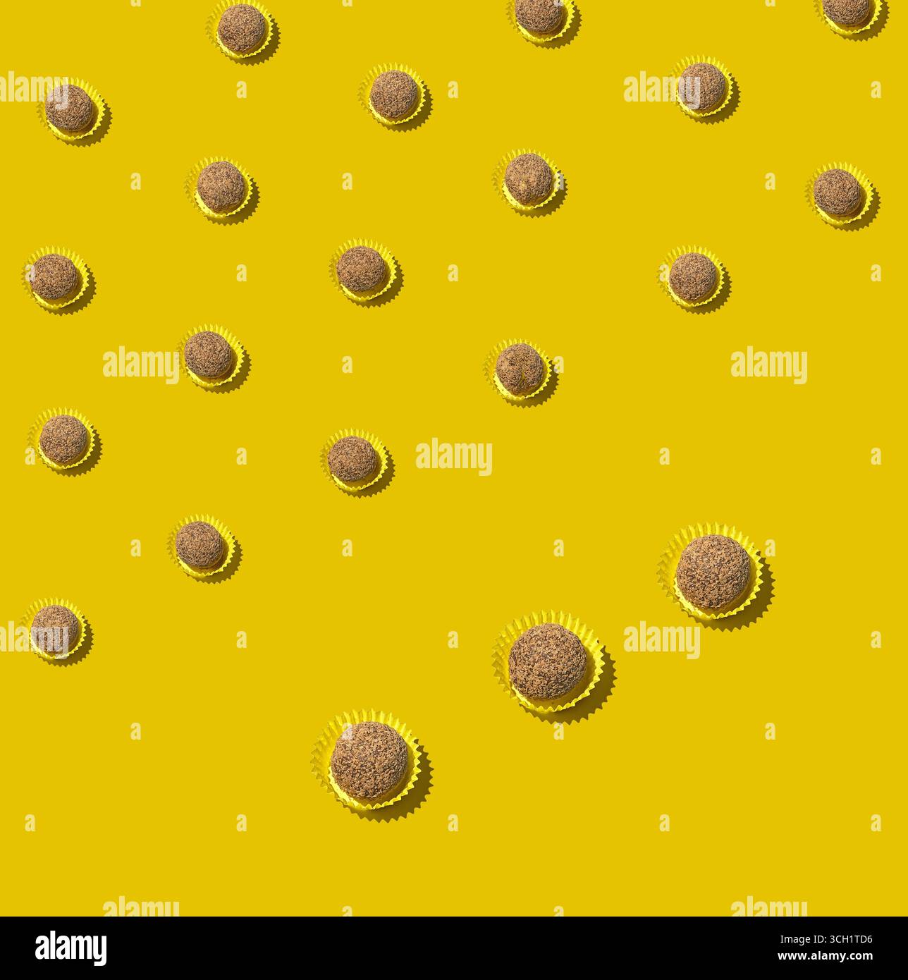 Ein stilles Leben über dem Kopf mit Schokoladentrüffelbonbons in Pappbechern, platziert in ordentlichen diagonalen Reihen auf einer lebhaften gelben Oberfläche mit verspieltem Minus Stockfoto