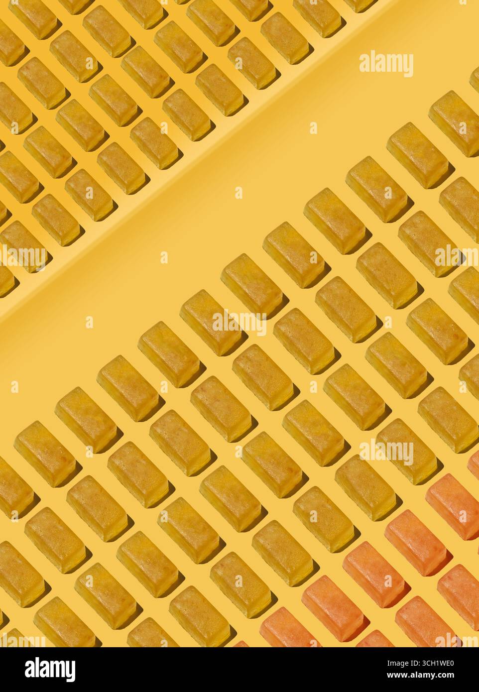 Ein künstlerisches Lebensmittelfoto mit Reihen von goldenen Gelee-Bonbons, die diagonal über einer warmen gelben Oberfläche angeordnet sind, schafft einen modernen, minimalen Konditor Stockfoto