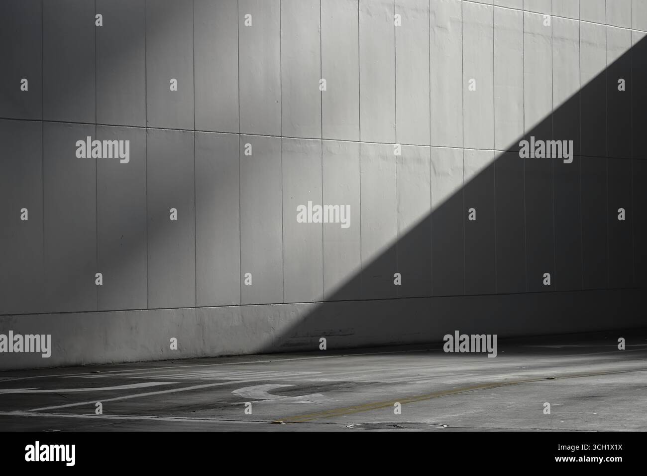 Einfache leere graue Betonwand und leere Stadtstraße mit Sonnenlicht und diagonalem Schatten. Stockfoto