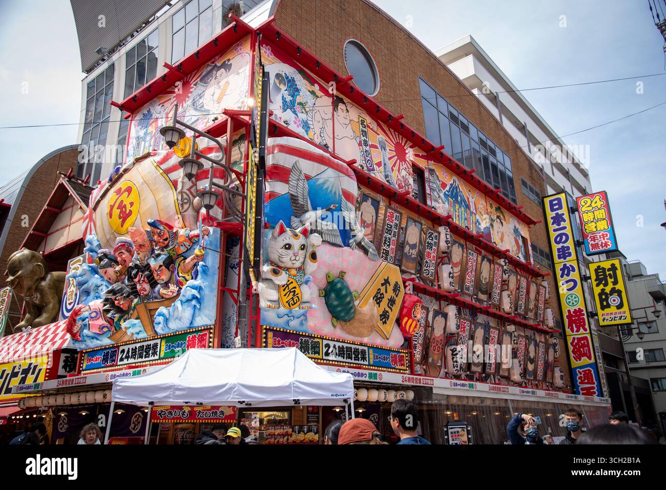 Hell dekorierte Fassade des Shinsekai-Restaurants mit Laternen, Glückskatzenstatue und farbenfroher japanischer Straßenkunst in Osaka, Japan. Stockfoto